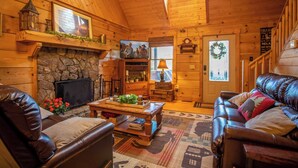 Un acogedor interior de cabaña de madera con chimenea de piedra, muebles de cuero y techo de madera.