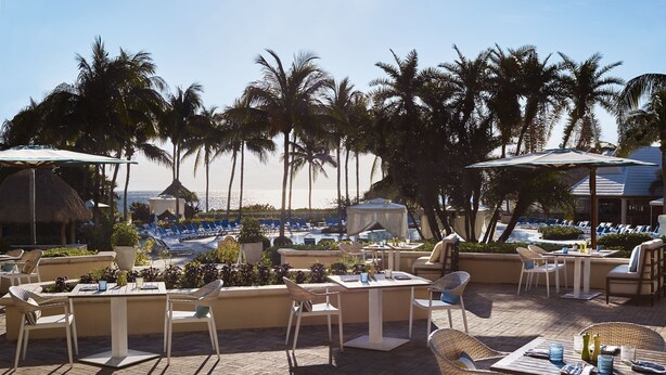 Un espace extérieur aménagé pour les repas, avec des tables et des chaises, offrant une vue sur une piscine et une plage.
