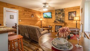 A cozy living room with a sofa, a dining table with a vase, a fireplace, and a television.