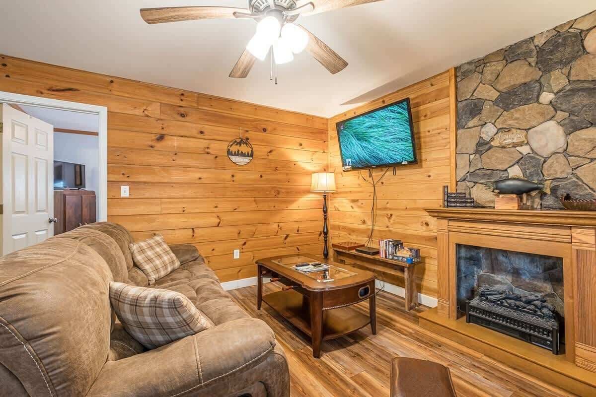 Un salon chaleureux avec un mur en bois, une cheminée, un téléviseur et un ventilateur de plafond.