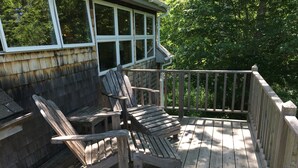 Um deck de madeira com cadeiras Adirondack e uma pequena mesa, cercado por um corrimão de madeira.