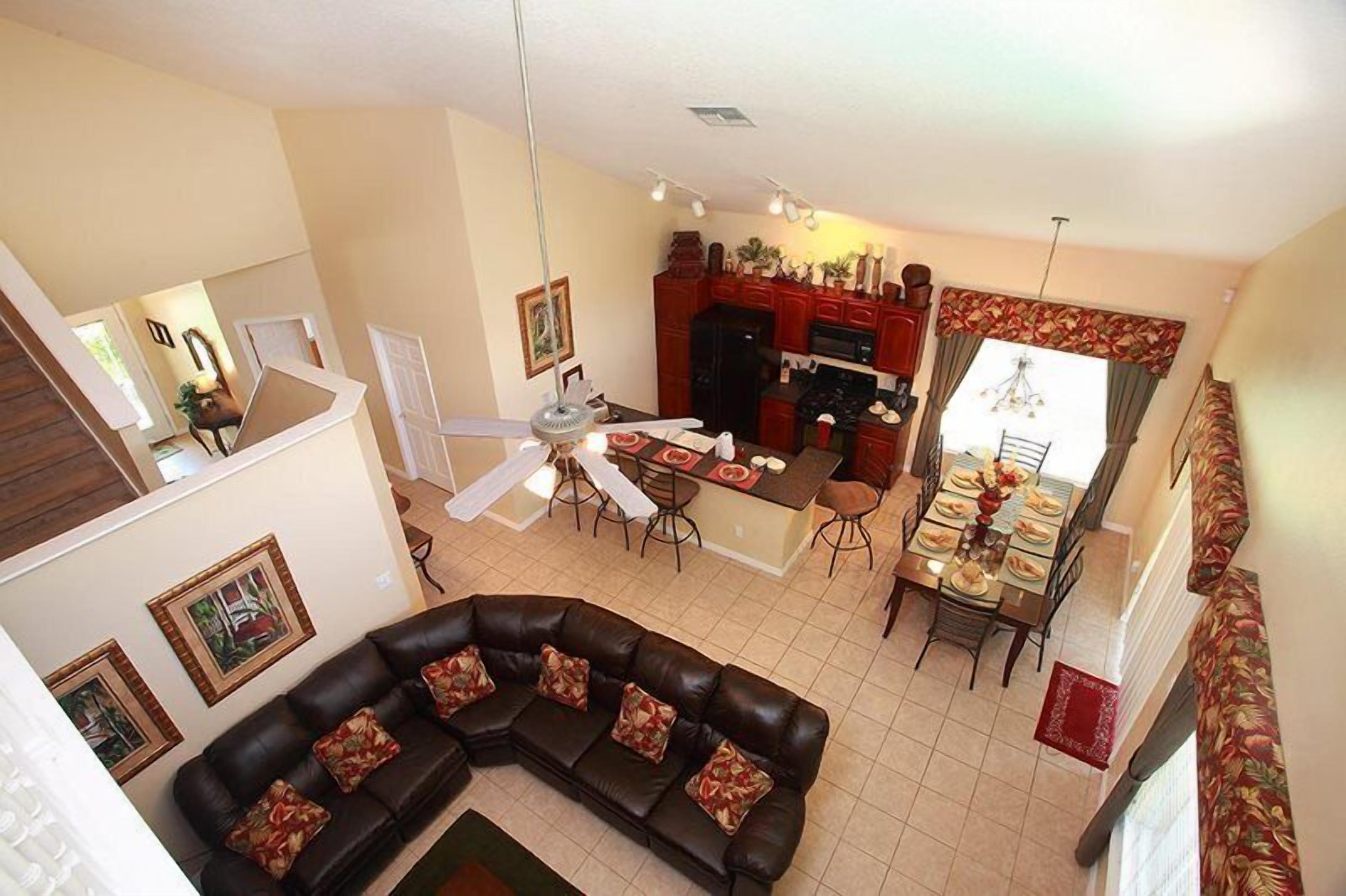 A spacious living area with a black leather sofa, a dining table set for four, and a kitchen in the background.