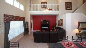 A spacious living room with a high ceiling, a balcony, a dining area with a table and chairs, and a red accent wall. - Ly230329 - Arcadia Estates - 7 Bed 6.5 Baths Villa (Kissimmee)