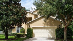 A residential house with a beige exterior, a white garage door, and a well-maintained lawn. - Ly230329 - Arcadia Estates - 7 Bed 6.5 Baths Villa (Kissimmee)