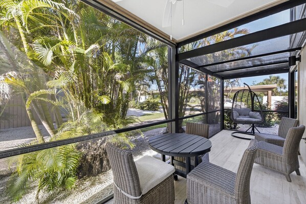 A covered outdoor patio with wicker furniture, a round table, and a hanging chair.