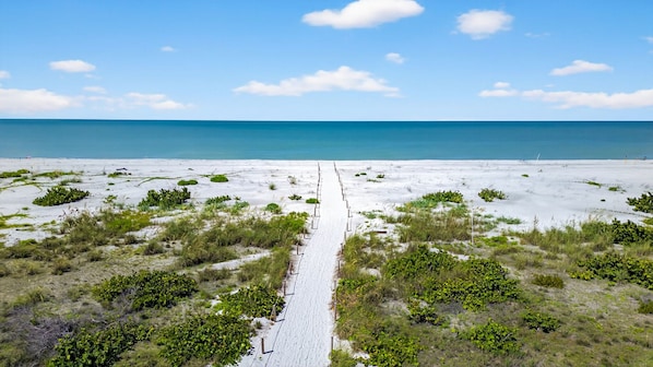 Una spiaggia con un sentiero sabbioso che conduce all'oceano, circondata da vegetazione rada.