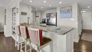 Una cocina moderna con armarios blancos, un refrigerador de acero inoxidable y una encimera de mármol.