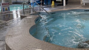 Piscina interior com tobogã aquático, rodeada por pavimento cerâmico e placas de segurança.