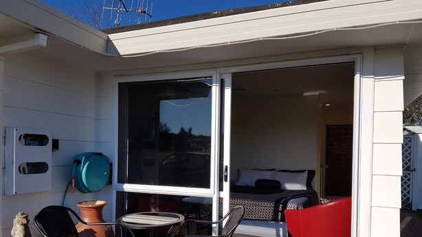 A patio with a table and chairs, a water heater, and a bed with a red chair. - Annandale Accommodation (Taupo)
