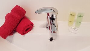 A bathroom sink with a chrome faucet, a red towel, and two bottles of shower gel. - Annandale Accommodation (Taupo)