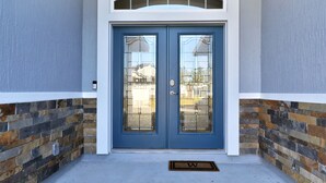 A blue double door with glass panels, a stone-patterned wall, and a small porch area with a doormat. - 3 bedroom ranch near Jax airport this charming home is set up for play or work. (Jacksonville)