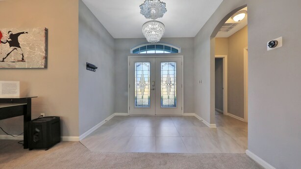 A spacious hallway with a chandelier, a door with glass panels, and a small desk with a computer. - 3 bedroom ranch near Jax airport this charming home is set up for play or work. (Jacksonville)