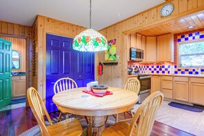 Un interno in legno con un tavolo da pranzo rotondo, sedie, una porta blu, una cucina con forno a microonde e uno schienale colorato.