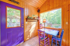 A cabin interior with a purple door, a table with a checkered tablecloth, and a window with a view of trees. - North Carolina Escape w/ Deck, Grill & Fire Pit! (Bryson City)
