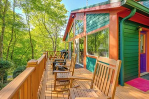 A wooden deck with outdoor seating, large windows, and a view of a forested area. - North Carolina Escape w/ Deck, Grill & Fire Pit! (Bryson City)