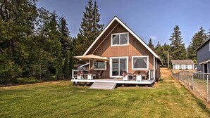 A modern two-story house with a large deck, a covered patio, and a view of the surrounding forest. - Modern Lake Lawrence Retreat w/ a Deck & Dock! (Yelm)