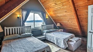 A cozy cabin bedroom with two beds, a large window with curtains, and a view of the water. - Modern Lake Lawrence Retreat w/ a Deck & Dock! (Yelm)