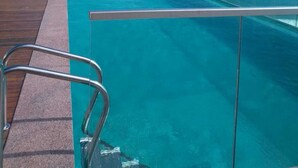 Une piscine à débordement offrant une vue imprenable sur l’océan, une terrasse en bois et une balustrade en verre.