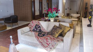 Un salon moderne avec un canapé beige, un plaid à motifs et un vase rempli de fleurs rouges.