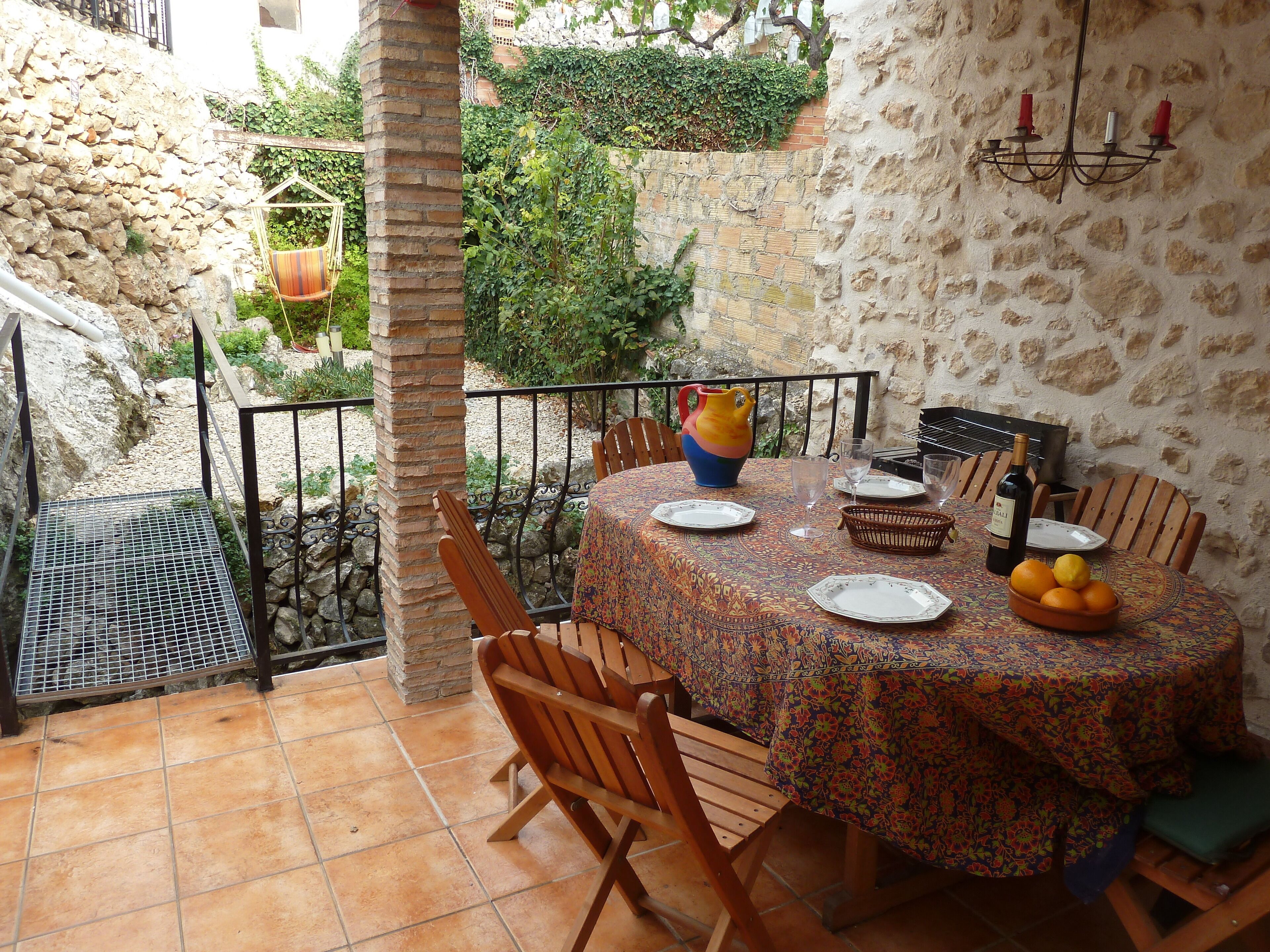 Une terrasse extérieure avec une table ronde dressée pour le repas, entourée de murs en pierre et de verdure.