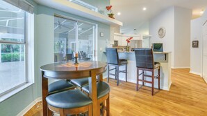 A modern kitchen with white cabinets, a wooden dining table with four chairs, and a small island with a sink and bar stools.