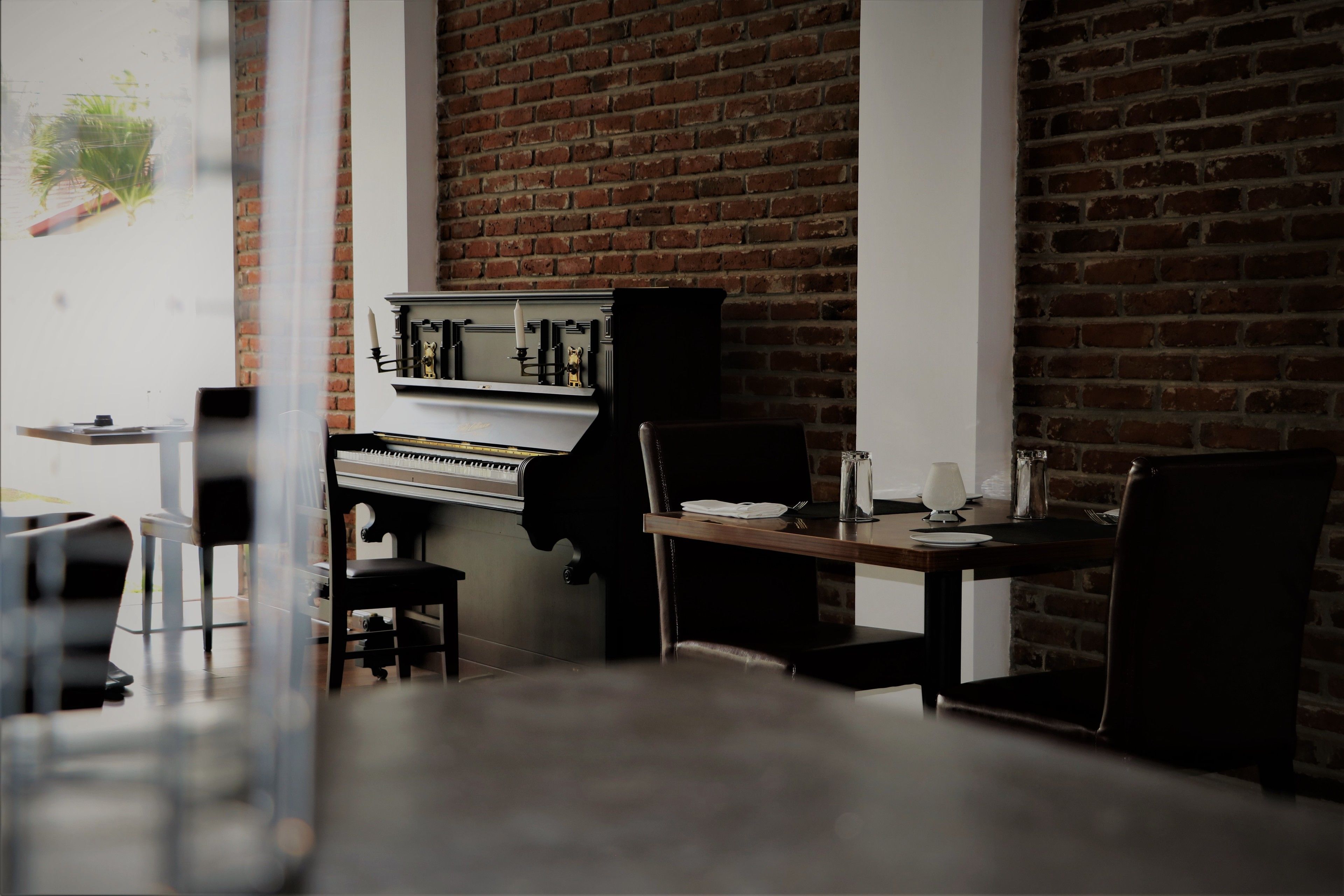 A dining area with a piano, a brick wall, and a table with chairs.