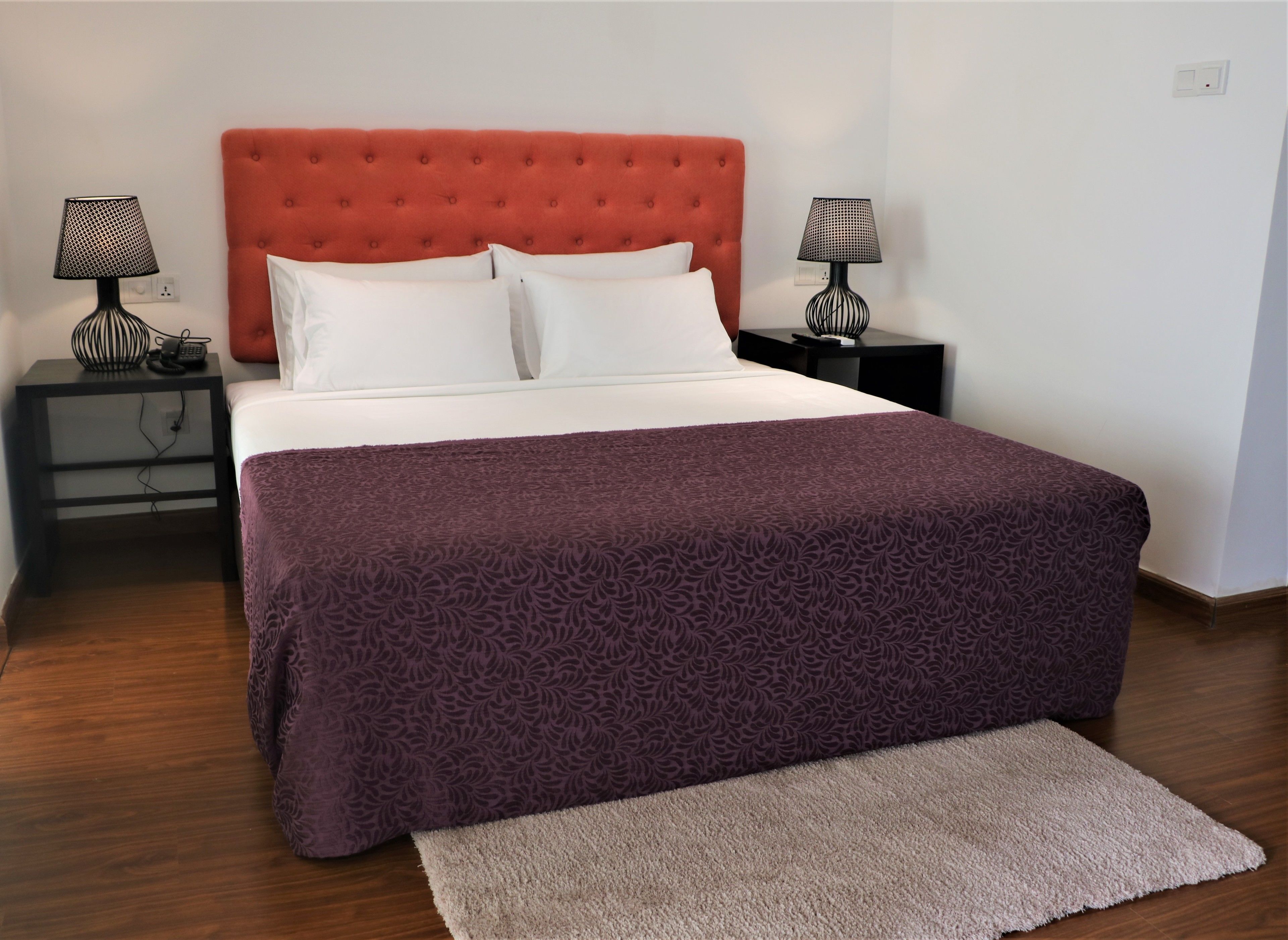 A neatly made bed with a patterned bedspread, two bedside tables with lamps, and a rug on the floor.