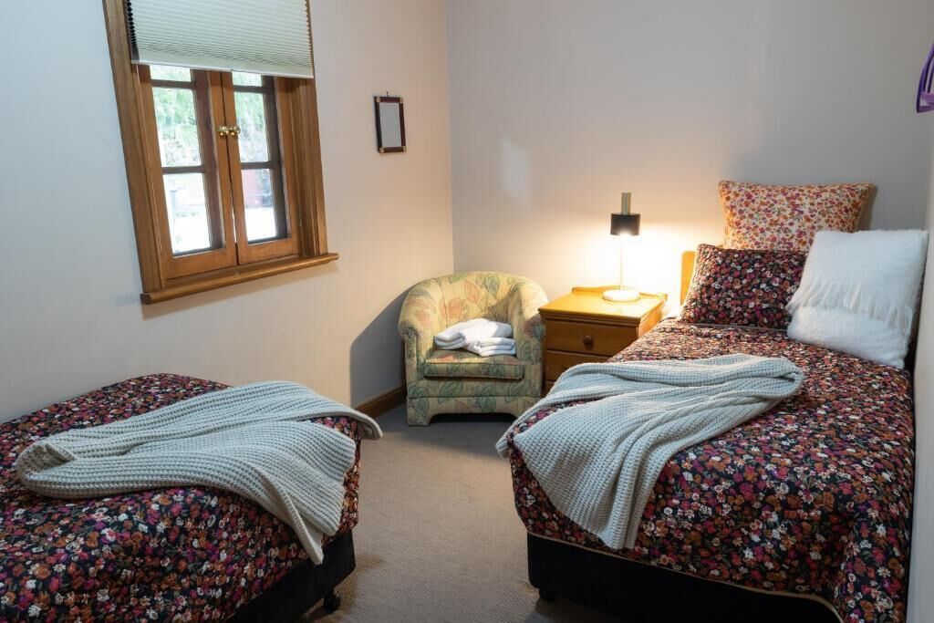 Una camera da letto con due letti singoli, una sedia, un comodino e una finestra con persiane.