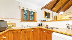 Una cocina con armarios de madera, un lavavajillas blanco y una ventana con persianas.