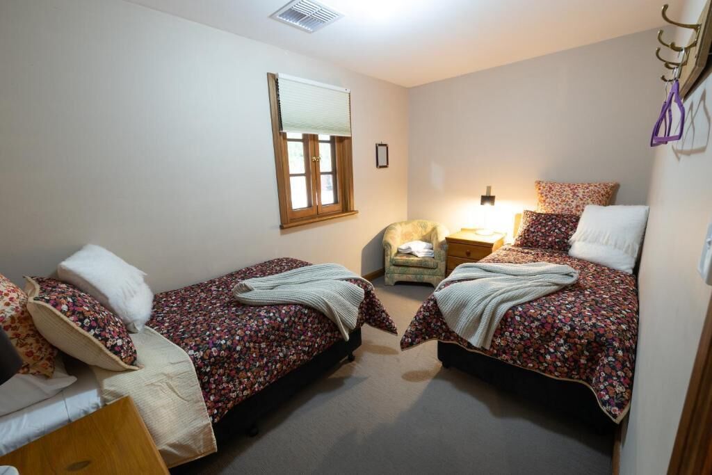 A bedroom with two single beds, a chair, a bedside table, and a window with blinds.