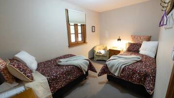 A bedroom with two single beds, a chair, a bedside table, and a window with blinds.