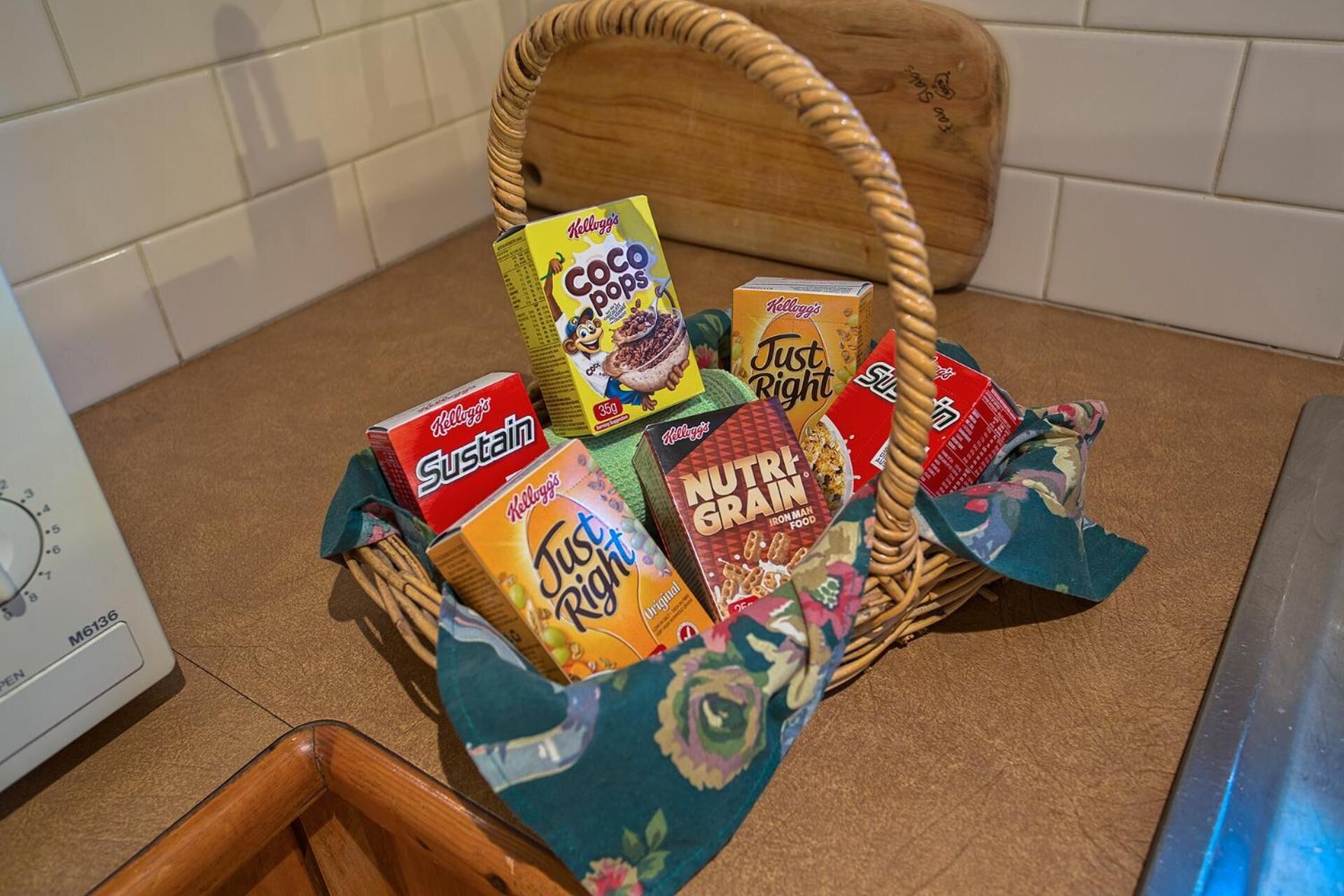 Una cesta de mimbre llena de varias cajas de cereales Kellogg's sobre una encimera de cocina.