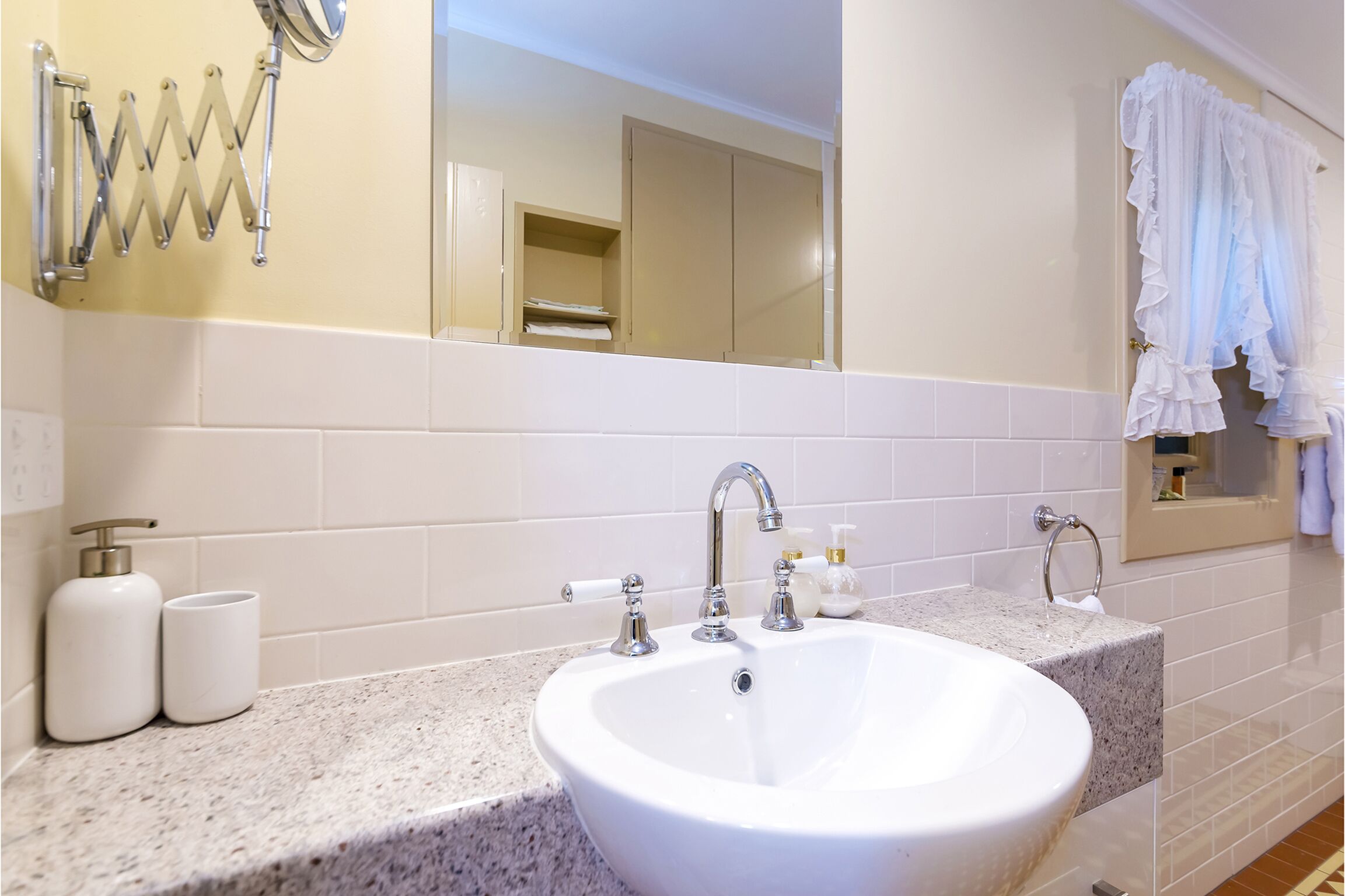A bathroom with a white sink, two faucets, a mirror, and a towel rack.