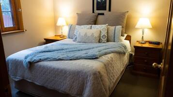 A bedroom with a bed, two bedside tables, a nightstand, a lamp, and a framed picture on the wall.