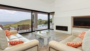 A modern living room with a large TV, two sofas with orange pillows, a coffee table, and a view of a pool and hills. - Holiday rental villa with swimming pool in Begur, Casa de camp (Begur)