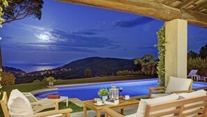 A poolside area with wooden furniture, a table with a drink, and a view of a mountainous landscape at night. - Holiday rental villa with swimming pool in Begur, Casa de camp (Begur)