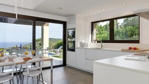 A modern kitchen with a large window, white cabinetry, and a dining area with a table and chairs. - Holiday rental villa with swimming pool in Begur, Casa de camp (Begur)