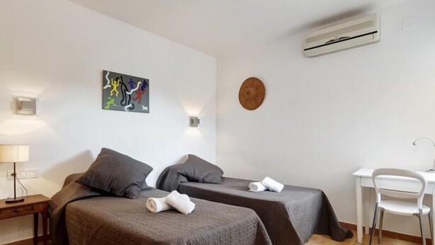 A hotel room with two beds, a desk, a chair, a wall-mounted air conditioner, and a wall art piece. - Holiday rental villa with swimming pool in Begur, Casa de camp (Begur)