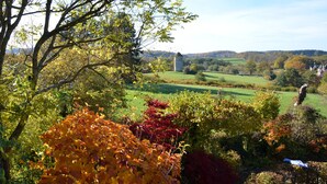A rural landscape with a tower, trees with autumn foliage, and a clear sky.