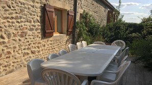 A stone building with a large outdoor dining area featuring a white table and plastic chairs.