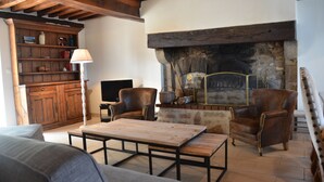 A cozy living room with a fireplace, leather armchairs, a wooden coffee table, and a bookshelf.