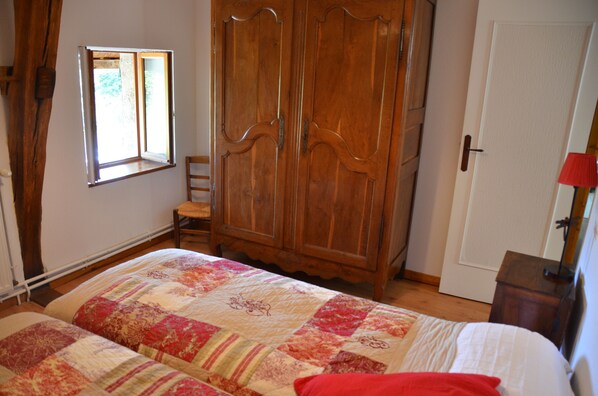 Ein Schlafzimmer mit großem Holzschrank, einem Fenster, einem Bett mit Steppdecke und einem Sessel.