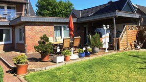 Ein zweistöckiges Haus mit überdachter Veranda, Blumentöpfen und Gartenmöbeln.