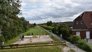 Ein Spielplatz mit Schaukeln und Rutschen, umgeben von Häusern und einem Fußweg.