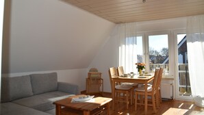 Ein Essbereich mit Holztisch und Stühlen, einer Couch und einem Fenster mit Vorhängen.