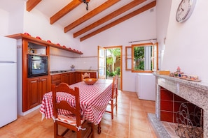 A kitchen with wooden beams, a dining table with a checkered tablecloth, and a view of greenery outside.