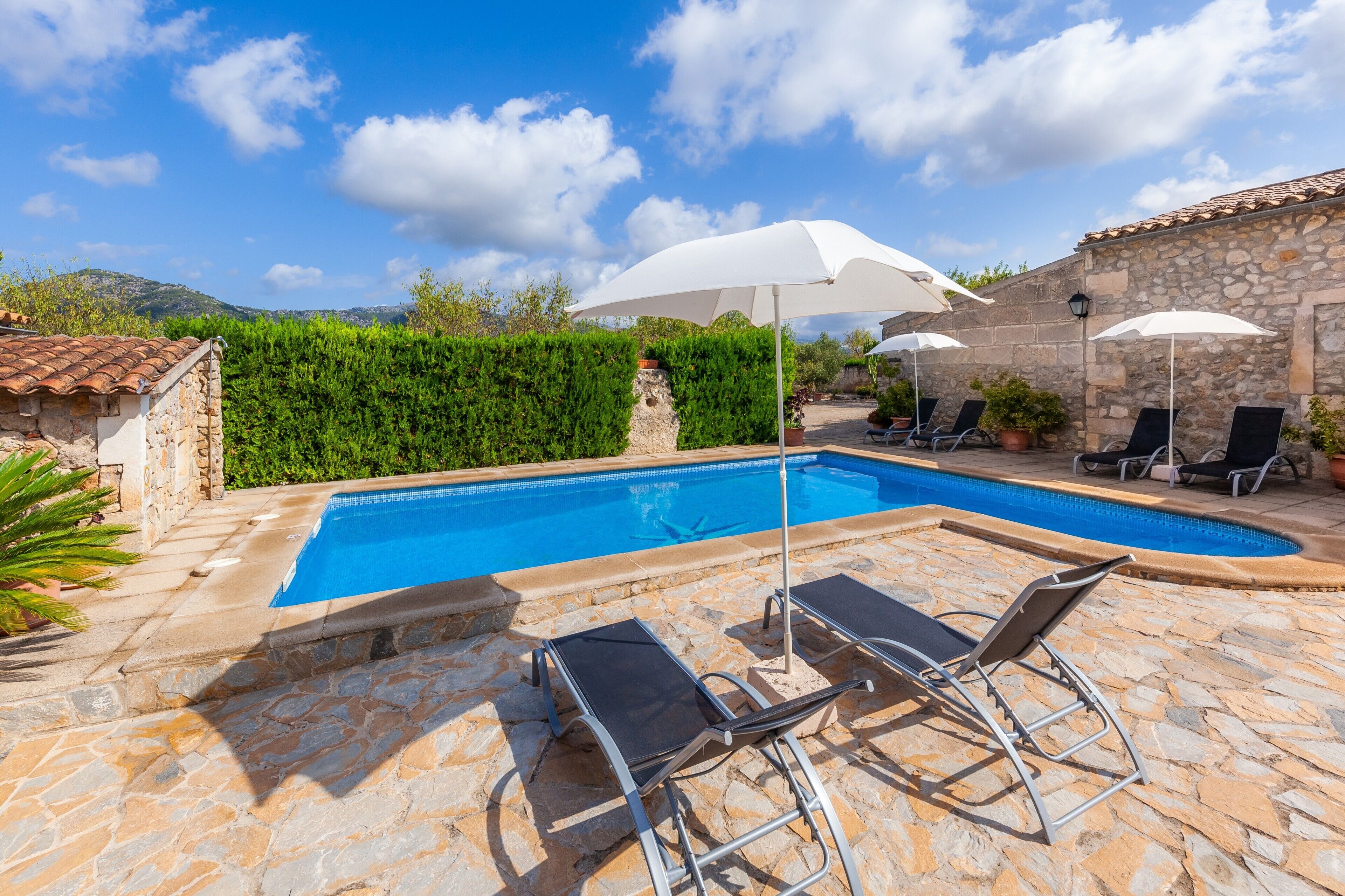 Una piscina con suelo de piedra, sillones de descanso y sombrillas.