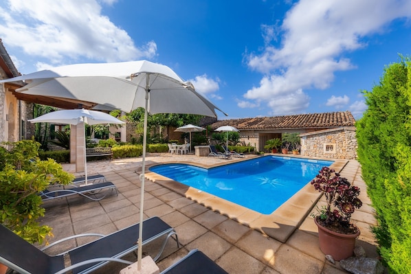 A swimming pool with lounge chairs and umbrellas, surrounded by stone walls and greenery.