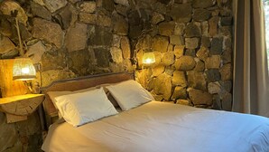 A bed in a room with stone walls and a wooden headboard. There are two bedside lamps and a wooden nightstand with a lamp. - Cabin between Forest and River  (Lo Barnechea)