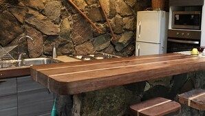 A kitchen with a stone wall, wooden utensils, a white refrigerator, and a wooden bar counter. - Cabin between Forest and River  (Lo Barnechea)